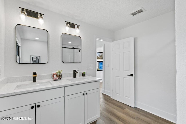 full bathroom with a textured ceiling, wood finished floors, visible vents, and a sink