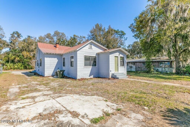 view of front of house featuring a chimney, entry steps, metal roof, and a front lawn