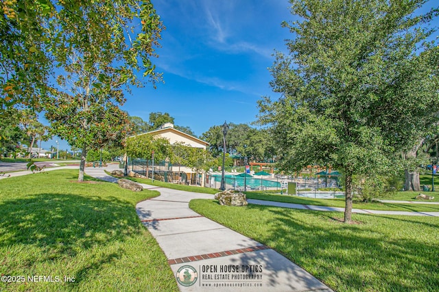 view of home's community with a swimming pool, a lawn, and fence