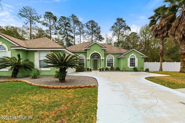 view of front of property featuring stucco siding, a front lawn, driveway, fence, and roof with shingles