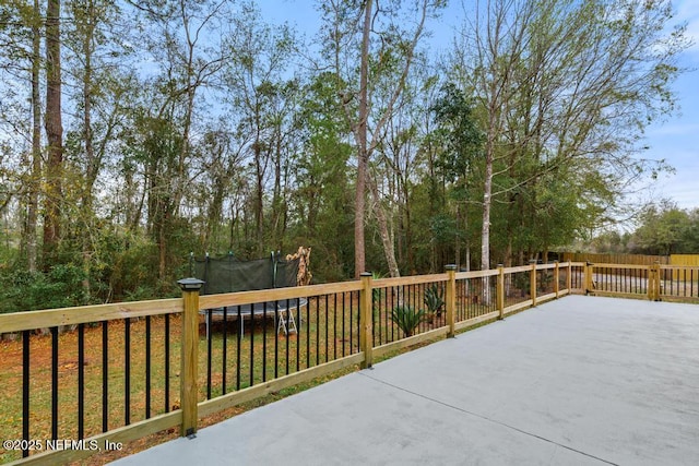 wooden terrace featuring a patio, a trampoline, and fence