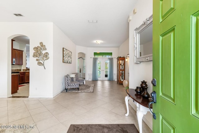 entrance foyer featuring visible vents, french doors, arched walkways, light tile patterned floors, and baseboards