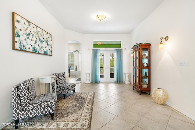 living area with light tile patterned floors, french doors, arched walkways, and baseboards