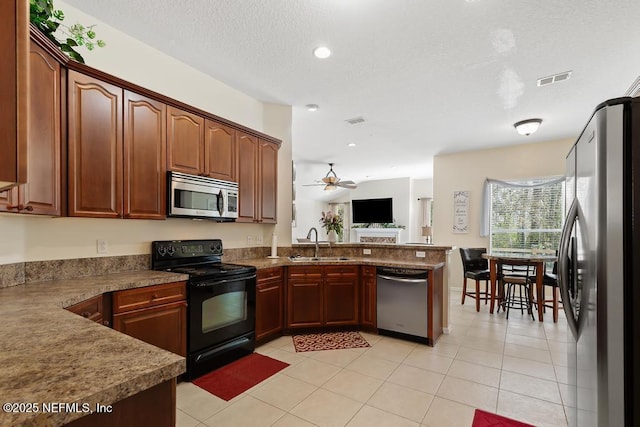 kitchen featuring a sink, a textured ceiling, stainless steel appliances, a peninsula, and light tile patterned flooring