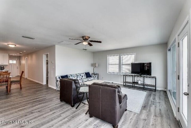 living area with light wood finished floors, a healthy amount of sunlight, baseboards, and ceiling fan