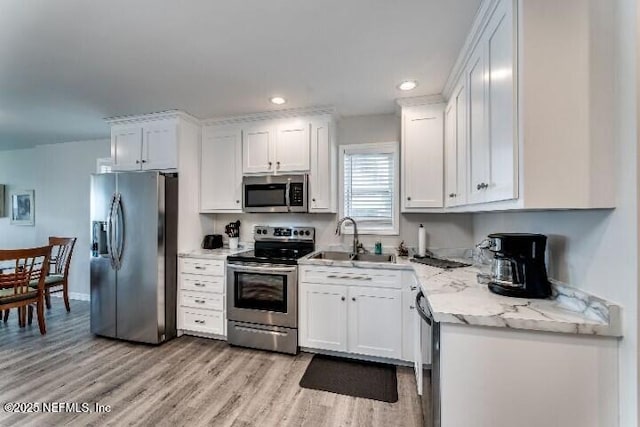 kitchen with light wood-type flooring, a sink, light stone counters, stainless steel appliances, and white cabinets