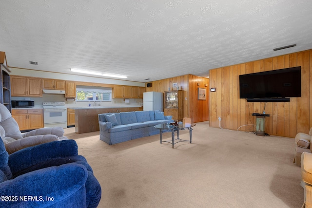 living area with light carpet, visible vents, wood walls, and a textured ceiling