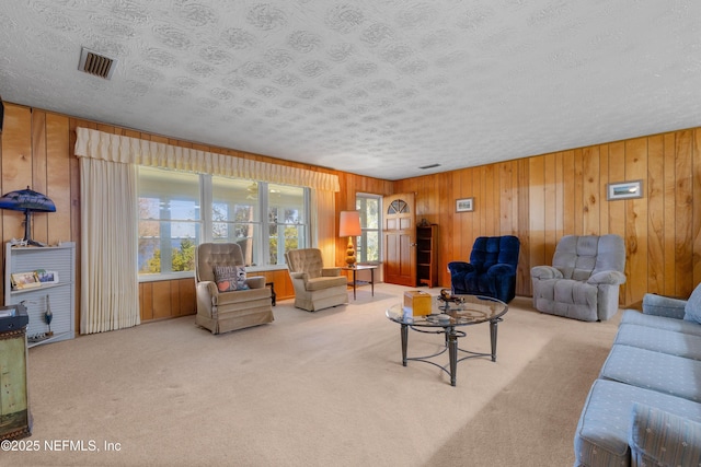 living area featuring wooden walls, carpet, visible vents, and a textured ceiling