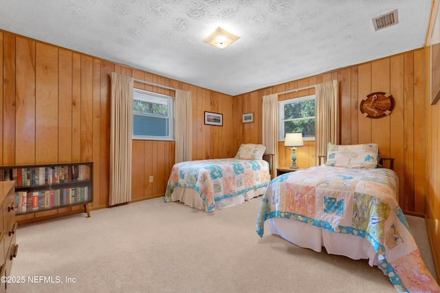 bedroom with visible vents, a textured ceiling, wood walls, and carpet flooring