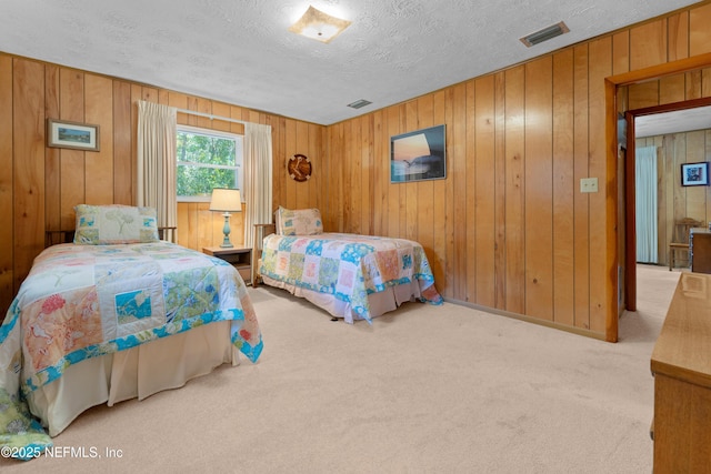 carpeted bedroom with visible vents, a textured ceiling, and wooden walls