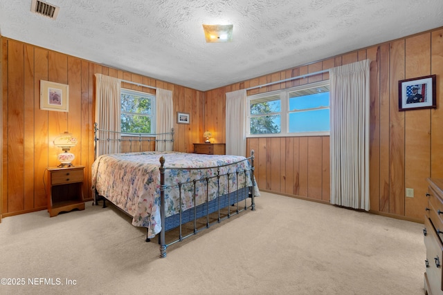 carpeted bedroom with baseboards, visible vents, wood walls, and a textured ceiling