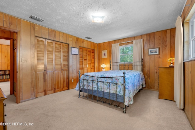 bedroom featuring visible vents, two closets, a textured ceiling, wooden walls, and carpet flooring