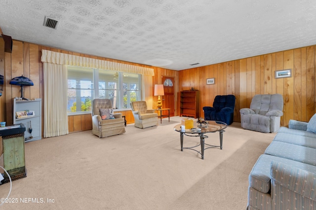 living room featuring visible vents, carpet floors, a textured ceiling, and wood walls