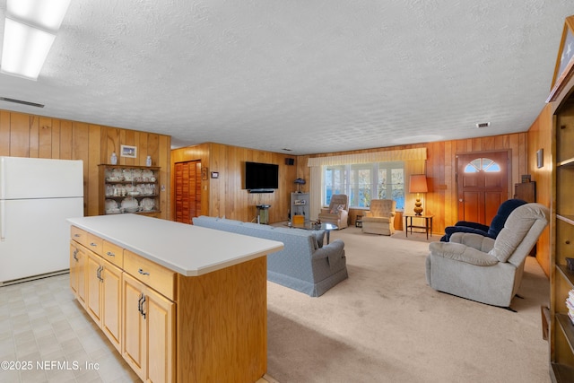 kitchen with wooden walls, freestanding refrigerator, light countertops, open floor plan, and a center island