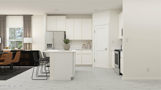 kitchen featuring stainless steel range with electric stovetop, a kitchen island with sink, a kitchen breakfast bar, white cabinetry, and white fridge with ice dispenser