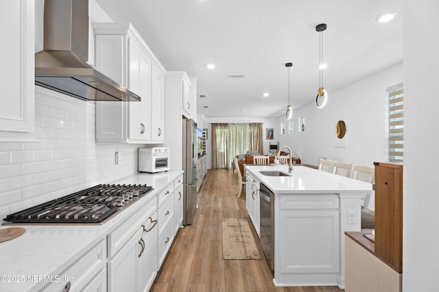 kitchen with light wood-type flooring, stainless steel appliances, white cabinetry, wall chimney exhaust hood, and tasteful backsplash