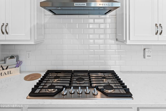 room details featuring decorative backsplash, range hood, white cabinets, and stainless steel gas stovetop