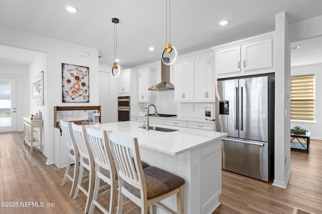 kitchen featuring an island with sink, a sink, tasteful backsplash, stainless steel appliances, and wall chimney exhaust hood