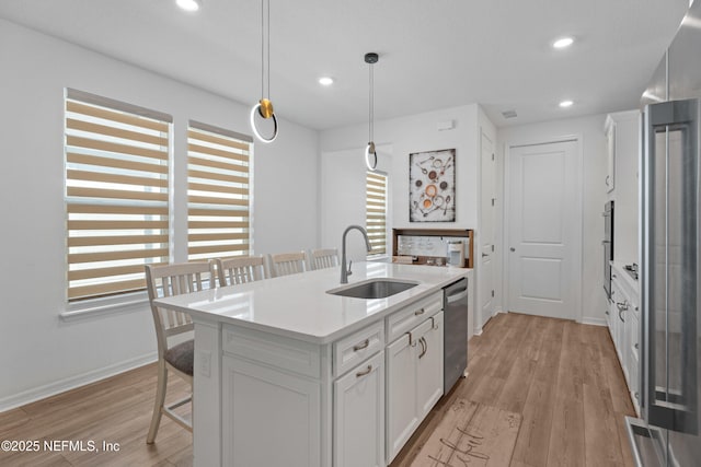 kitchen featuring a breakfast bar area, white cabinets, stainless steel dishwasher, and a sink