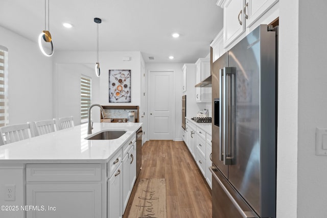 kitchen with an island with sink, a sink, white cabinetry, stainless steel appliances, and light countertops