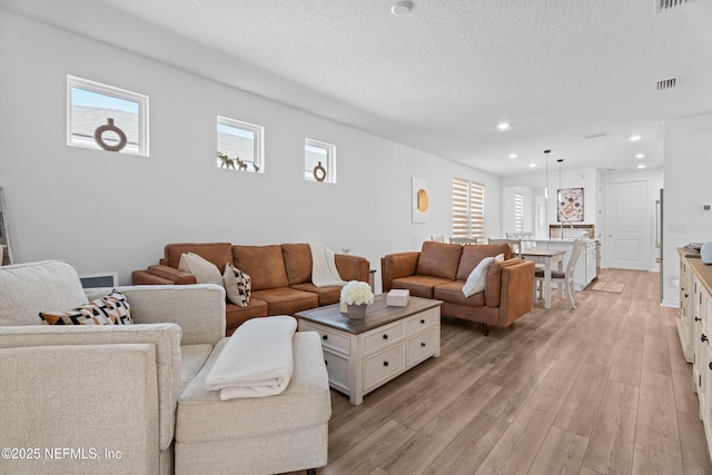 living room with a textured ceiling, a healthy amount of sunlight, visible vents, and light wood-type flooring