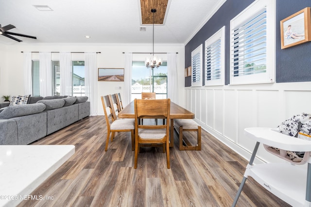 dining room featuring crown molding, ceiling fan with notable chandelier, visible vents, a decorative wall, and wood finished floors