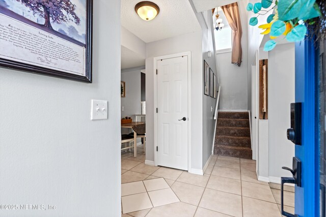 entryway featuring light tile patterned floors, baseboards, a textured ceiling, and stairs