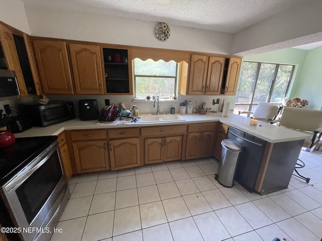 kitchen with a peninsula, stainless steel appliances, a sink, light countertops, and a textured ceiling