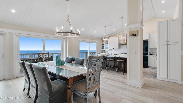 dining area featuring lofted ceiling, light wood-style flooring, recessed lighting, a water view, and a chandelier