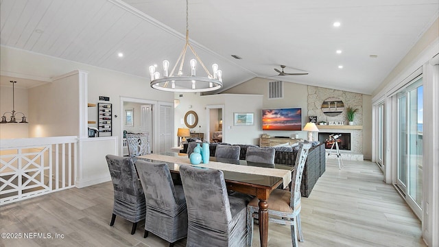 dining room featuring light wood-type flooring, visible vents, ceiling fan with notable chandelier, a fireplace, and lofted ceiling