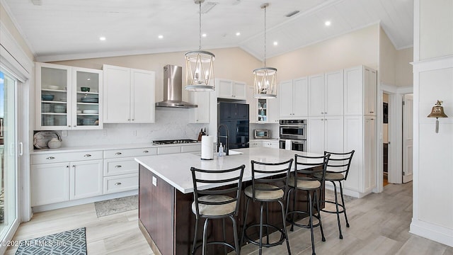 kitchen featuring a center island with sink, gas cooktop, double oven, wall chimney exhaust hood, and light countertops