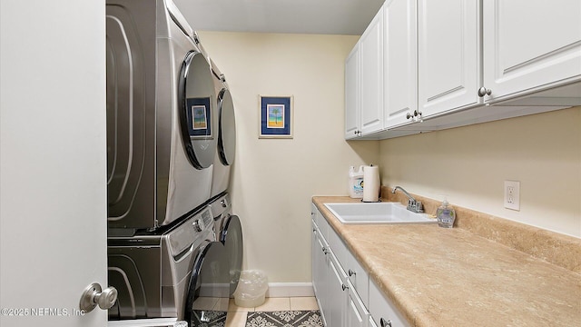 laundry area featuring baseboards, light tile patterned floors, stacked washer and clothes dryer, cabinet space, and a sink