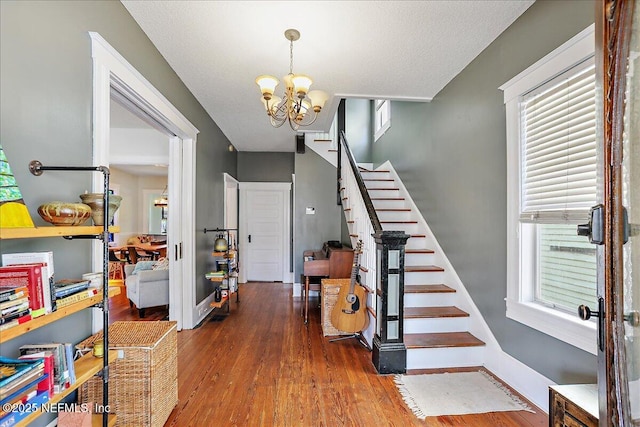 stairs featuring a notable chandelier, wood finished floors, baseboards, and a textured ceiling