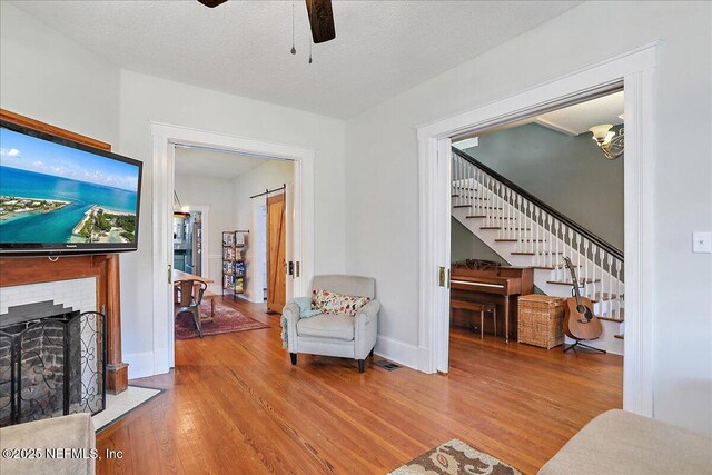 living room featuring a brick fireplace, stairway, wood finished floors, a textured ceiling, and a ceiling fan