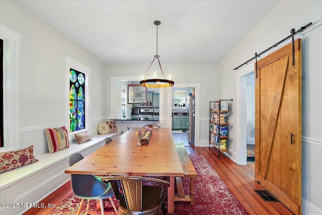 dining room featuring a barn door, a notable chandelier, wood finished floors, and visible vents