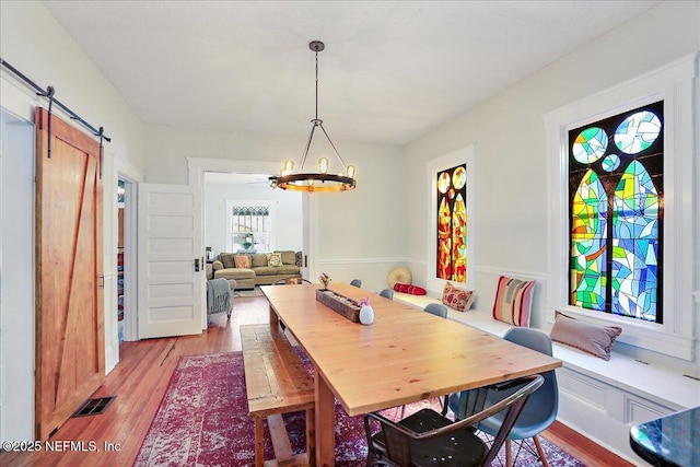 dining room with an inviting chandelier, a barn door, wood finished floors, and visible vents