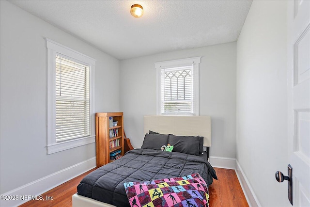 bedroom featuring a textured ceiling, baseboards, and wood finished floors