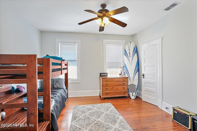 bedroom featuring ceiling fan, visible vents, baseboards, and wood finished floors