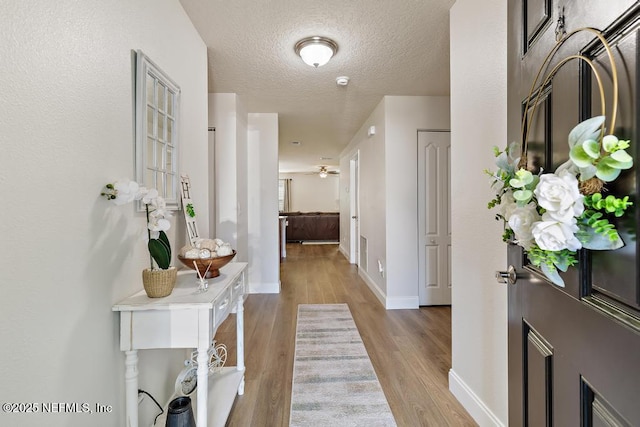 hallway with baseboards, a textured ceiling, and wood finished floors