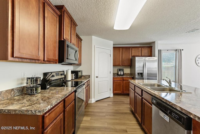 kitchen with visible vents, appliances with stainless steel finishes, light wood-style floors, brown cabinetry, and a sink