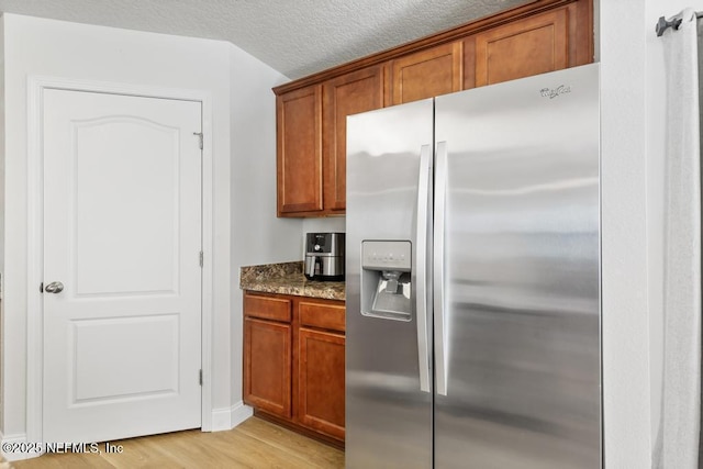 kitchen featuring dark stone countertops, brown cabinetry, stainless steel refrigerator with ice dispenser, and light wood-type flooring