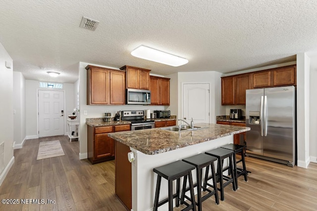 kitchen with light wood-type flooring, visible vents, brown cabinets, a sink, and stainless steel appliances