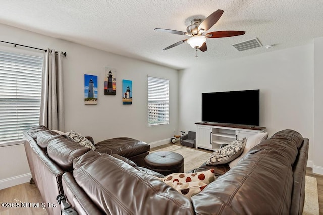 living area featuring visible vents, a ceiling fan, a textured ceiling, light wood finished floors, and baseboards