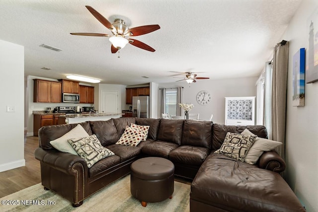 living room with visible vents, baseboards, a textured ceiling, and wood finished floors