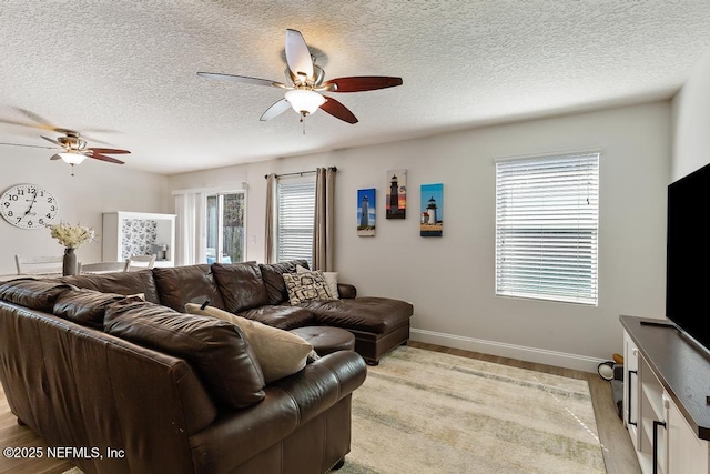 living room featuring baseboards, light wood-style floors, ceiling fan, and a textured ceiling