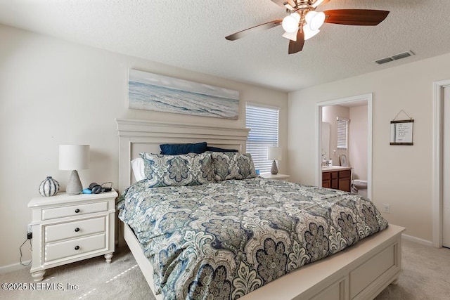 bedroom featuring visible vents, baseboards, light colored carpet, ensuite bathroom, and a textured ceiling