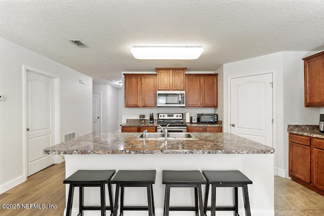 kitchen with visible vents, a kitchen breakfast bar, brown cabinetry, stainless steel appliances, and a sink