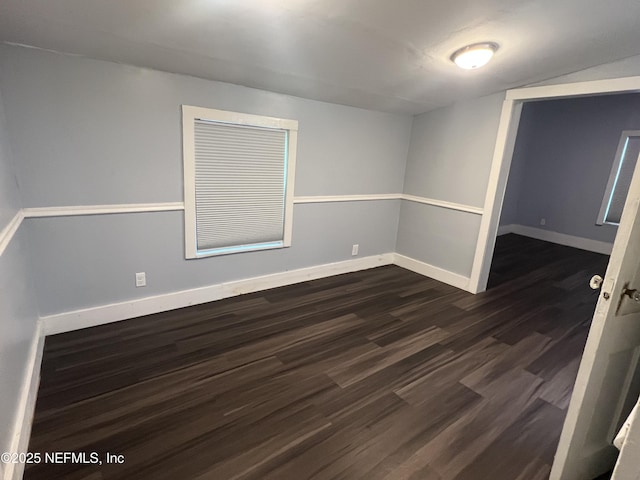 empty room featuring lofted ceiling, dark wood-style floors, and baseboards