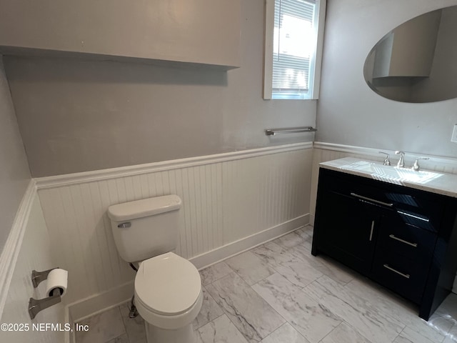 bathroom with vanity, toilet, marble finish floor, and wainscoting