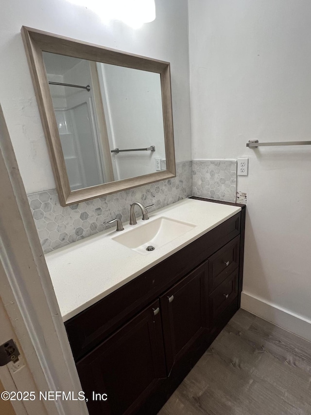 bathroom with backsplash, vanity, baseboards, and wood finished floors